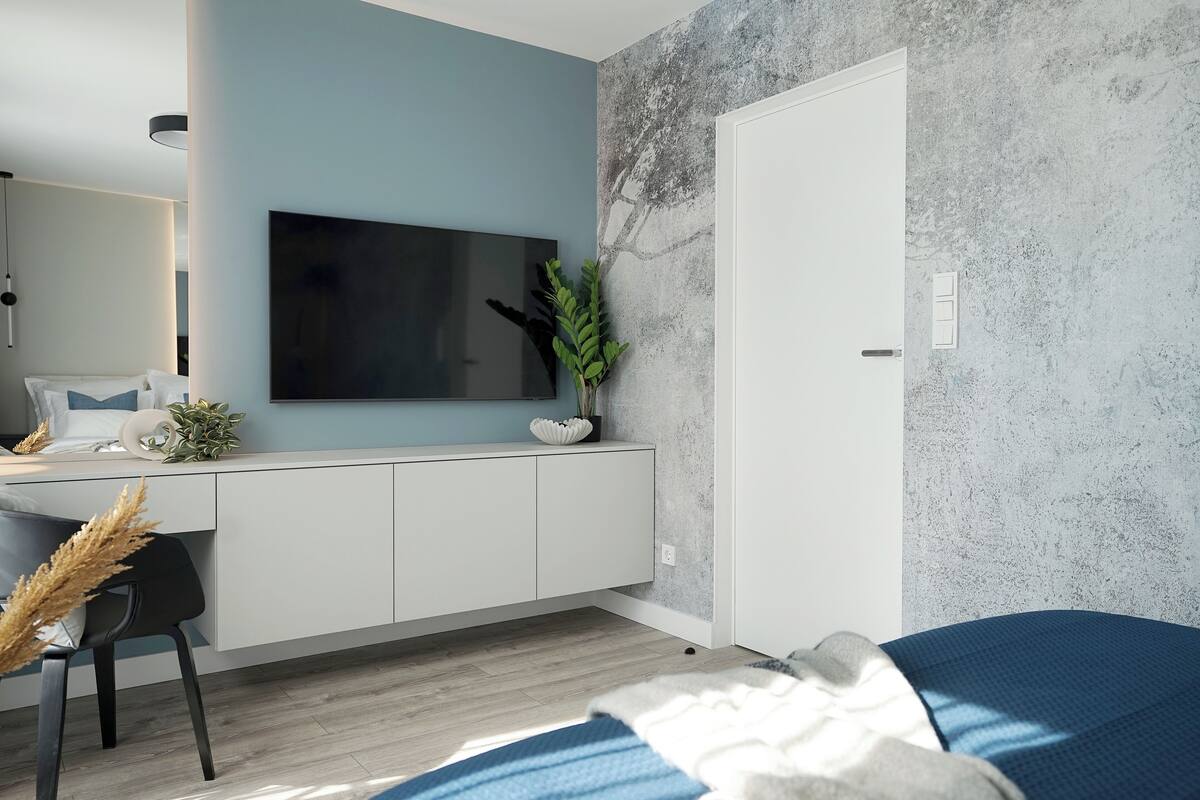 A modern bedroom with a bed, a desk, a chair, a TV, and a plant.