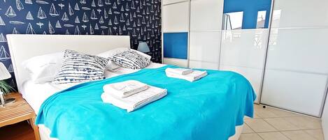 A neatly made bed with a blue bedspread and white pillows, a wooden nightstand with a lamp, and a wardrobe with blue panels.