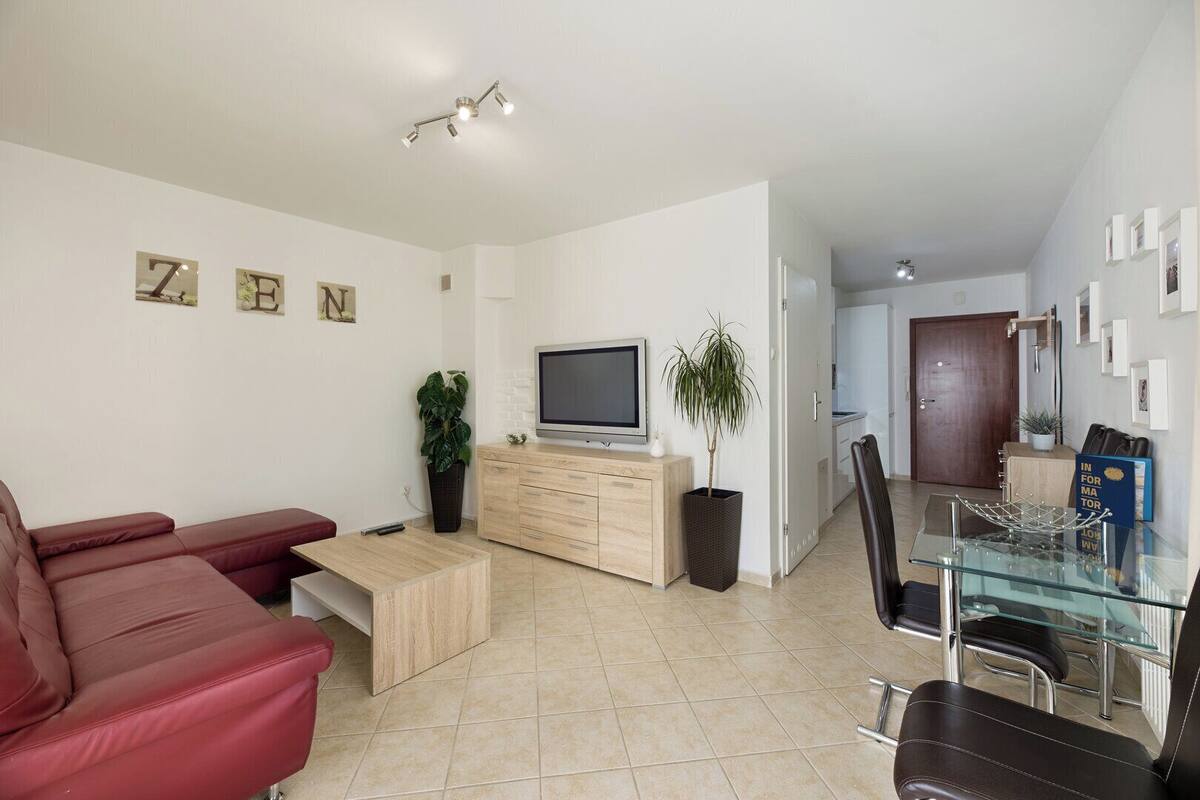 A modern living room with a red sofa, a glass dining table, and a TV on a wooden cabinet.