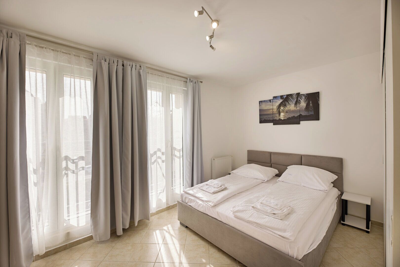 A hotel room with a large bed, a nightstand, a wall-mounted lamp, and a painting.