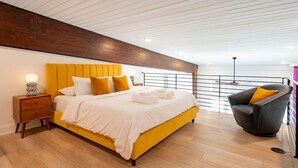 A modern bedroom with a large bed, a nightstand, a chair, and a view of the sea.
