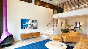 A modern living room with a large TV, a staircase, and a seating area with sofas and a coffee table.