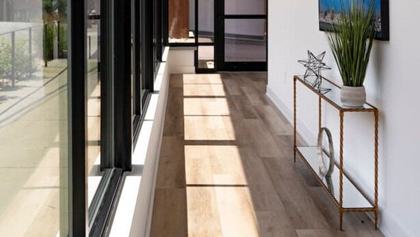 A modern hallway with large windows, a wooden floor, and a framed artwork on the wall.