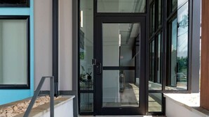 A modern building entrance with a glass door, a concrete staircase, and a metal handrail.