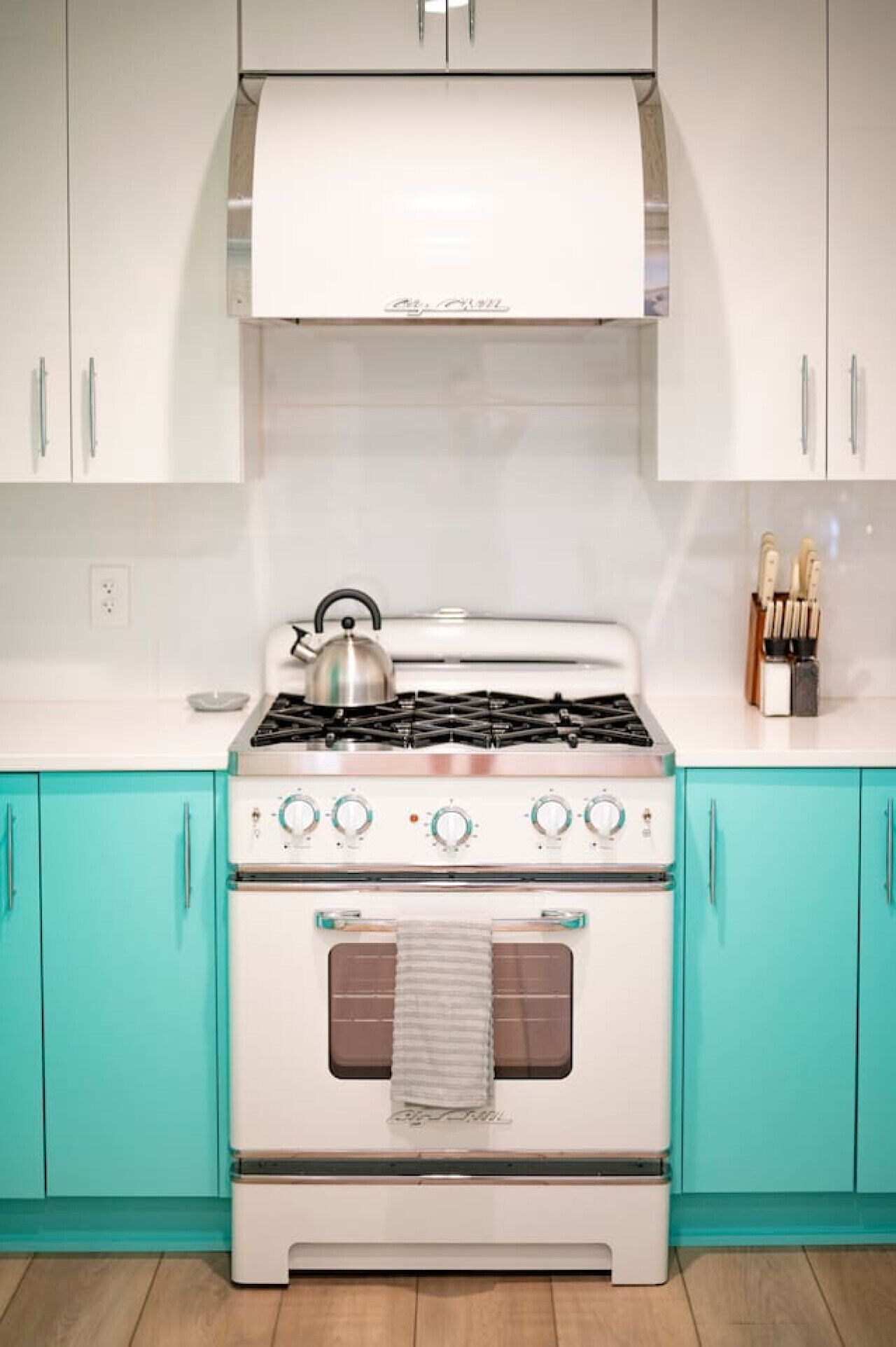A kitchen with a white stove, teal cabinets, and a white countertop.