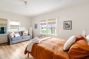 A bedroom with a bed, a sofa, a chair, and a window with a view.