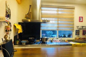 A kitchen with a stove, pots, and a window with blinds. - Mystery 13 Hostel (Yilan)