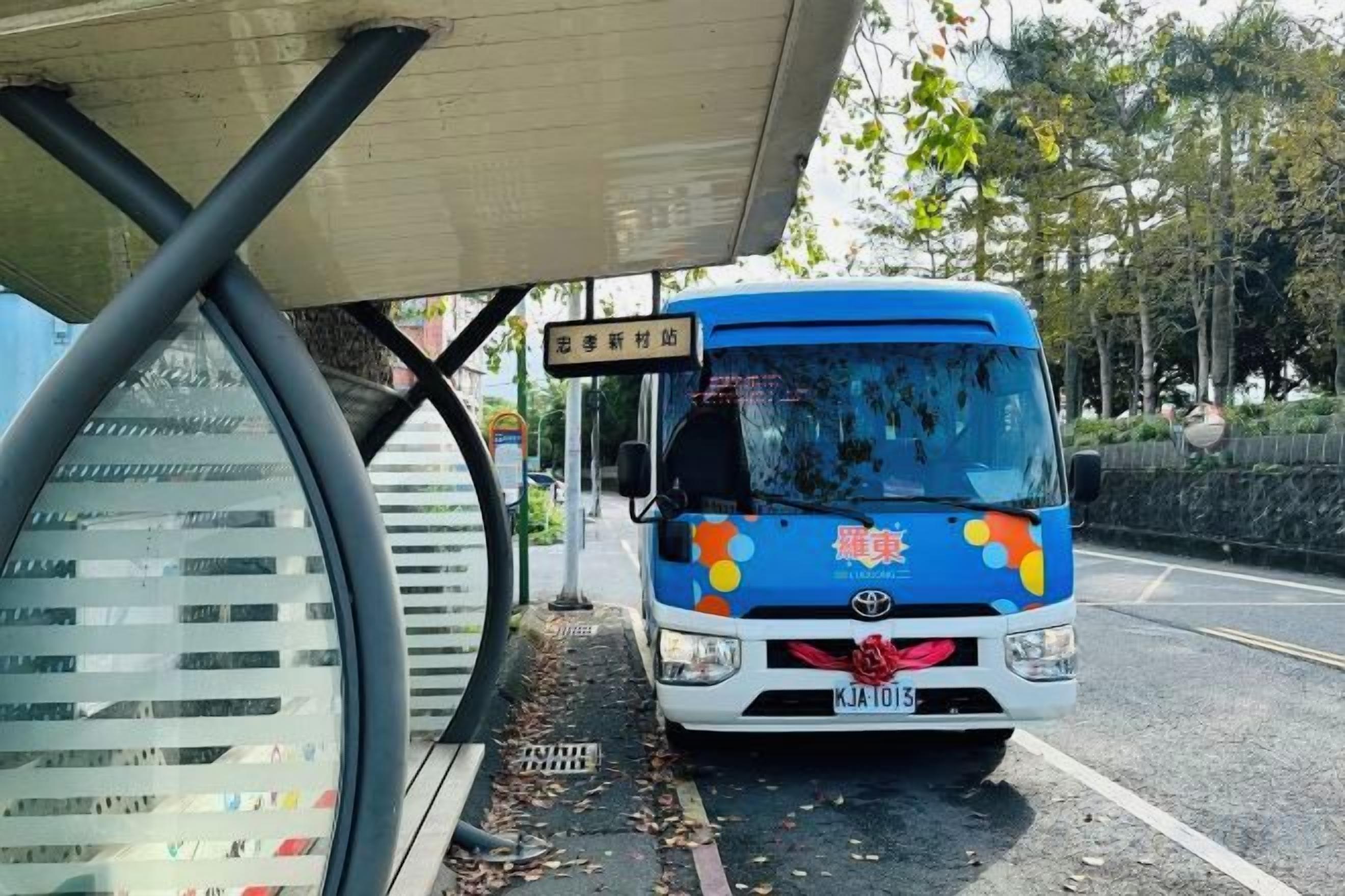 Un autobús azul estacionado bajo un refugio, con patente a la vista.