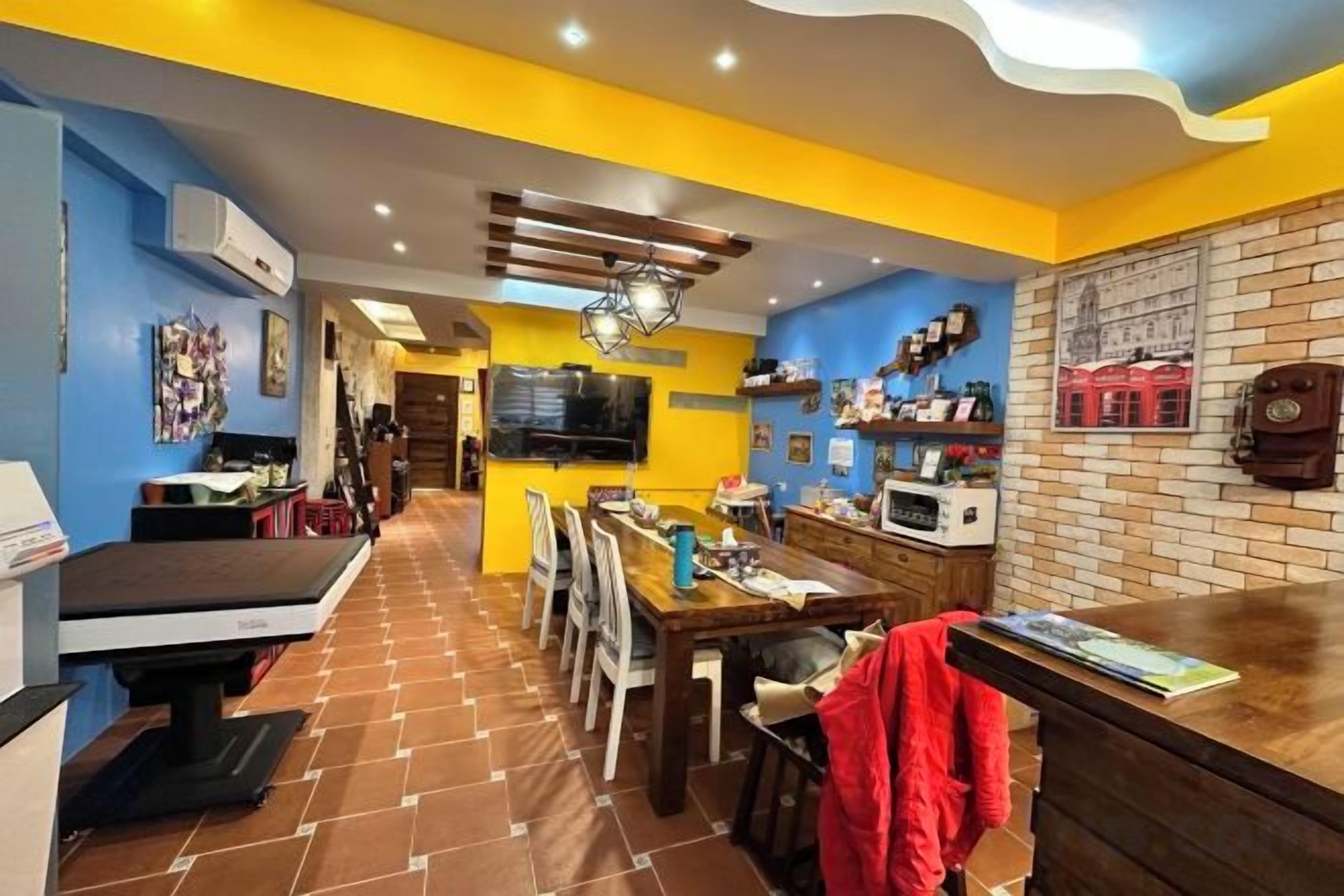 Une cuisine avec un coin repas, un téléviseur fixé au mur et un mur en briques avec des étagères.