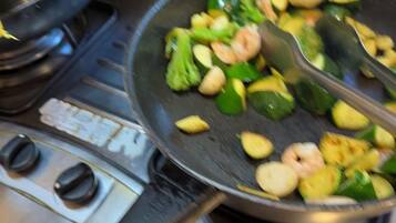 A kitchen with a frying pan on a stove, containing vegetables and shrimp.