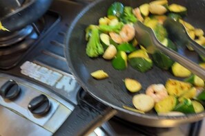 A kitchen with a frying pan on a stove, containing vegetables and shrimp. - Mystery 13 Hostel (Yilan)