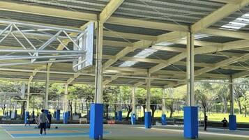 An outdoor basketball court with a covered roof, blue flooring, and several basketball hoops.