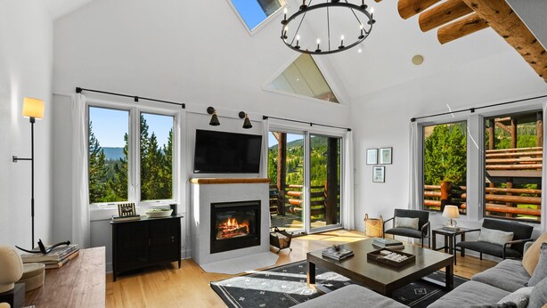 A spacious living room with a fireplace, large windows, and a modern chandelier.