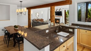 A modern kitchen with granite countertops, a built-in sink, and a wooden island. There is a dining area with a table and chairs, and a living room with a sofa and fireplace.