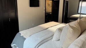 A bedroom with a bed, a television on the wall, and a door leading to another room.