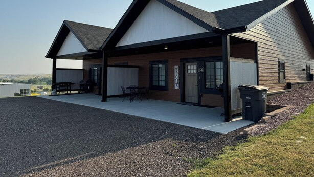 A modern building with a covered patio area, a welcome sign, and a trash bin.