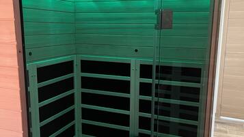 Een sauna met een glazen deur, groen licht en een handdoek op de vloer.