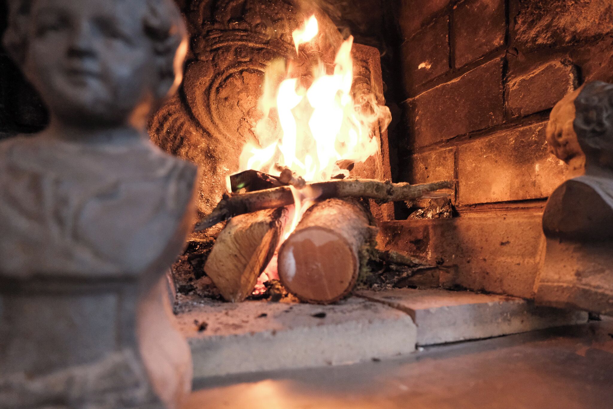 A fireplace with burning logs and a stone wall.
