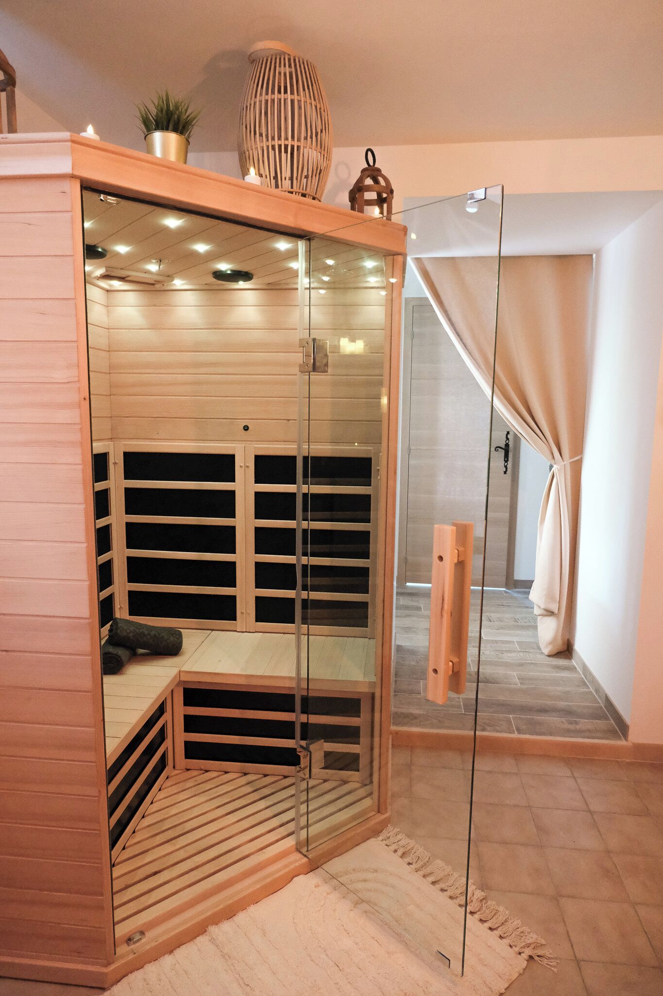 Una sala de sauna con puerta de vidrio, bancos de madera y una planta pequeña en la parte superior.