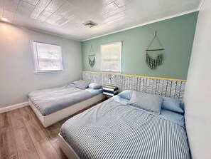 A room with two beds, each with striped bedding, a wooden floor, and a green wall with a decorative hanging. - Lakefront House with Water Toys : close to Camelback, Kalahari, Casino, Hiking! (Long Pond)