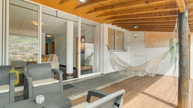 A modern interior with wicker furniture, a hammock, and a view through glass doors. - Alfa I in Machico With 2 Bedrooms and 2 Bathrooms (Machico)