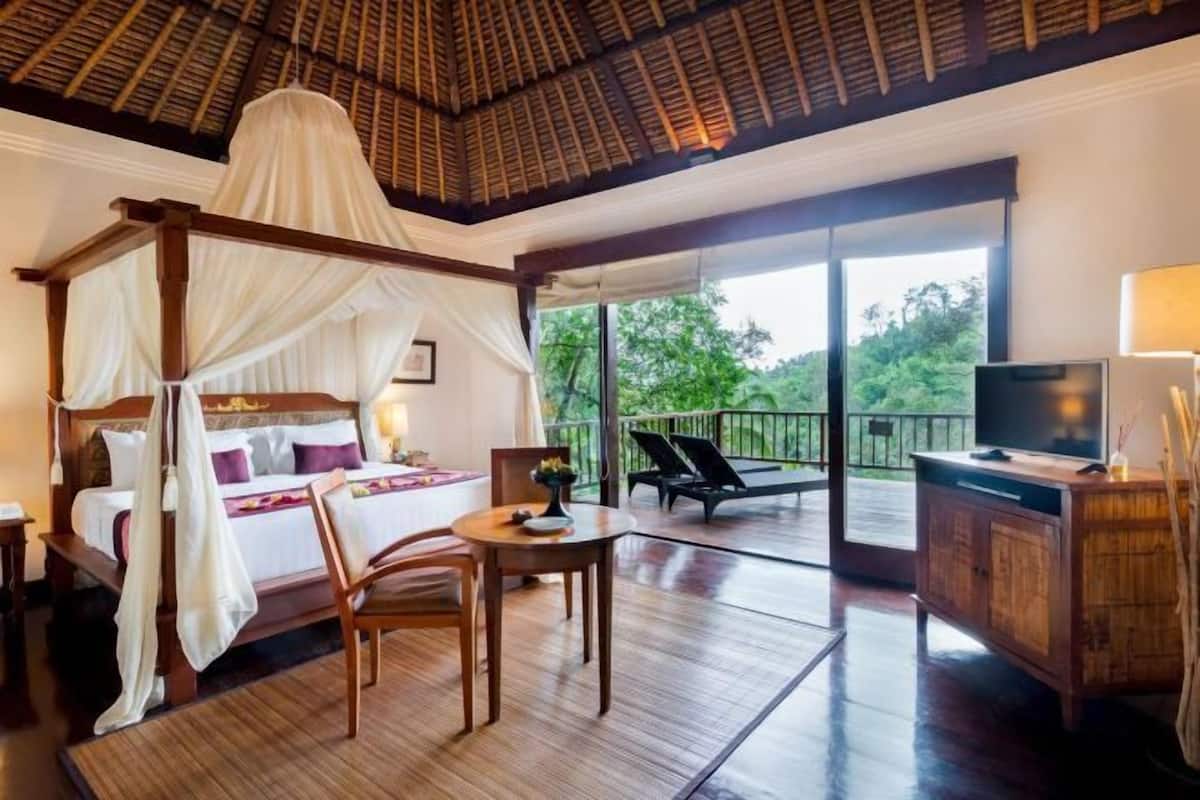 Un dormitorio con cama con dosel, televisión, mesa de comedor y balcón con sillas.