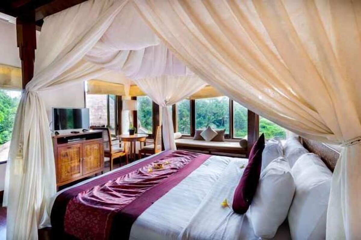 A bedroom with a canopy bed, a desk, and a television.