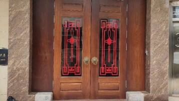 A wooden double door with intricate red designs, a stone wall to the left, and a small step leading up to the entrance.