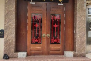 A wooden double door with intricate red designs, a stone wall to the left, and a small step leading up to the entrance. - Taichang Hotel (Yangjiang)