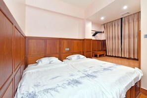 A bedroom with a wooden headboard, a bed with a floral bedspread, a bench, and a window with curtains. - Taichang Hotel (Yangjiang)