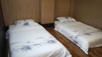 A room with two single beds, wooden flooring, and plain walls.