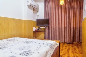 A hotel room with a bed, a television mounted on the wall, a wooden floor, and a curtain.