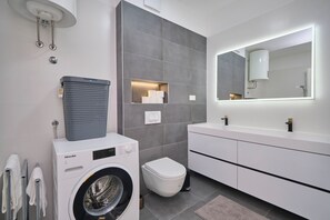 A modern bathroom with a washing machine, a toilet, a sink, and a large mirror. - Tropic Night Apartment by Litto (Split)