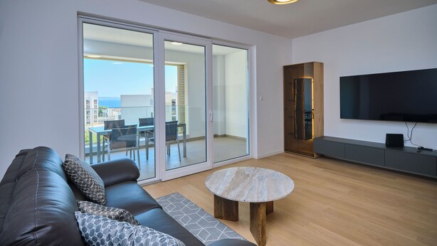 A modern living room with a leather sofa, a round coffee table, and a flat-screen TV mounted on the wall. - Tropic Night Apartment by Litto (Split)