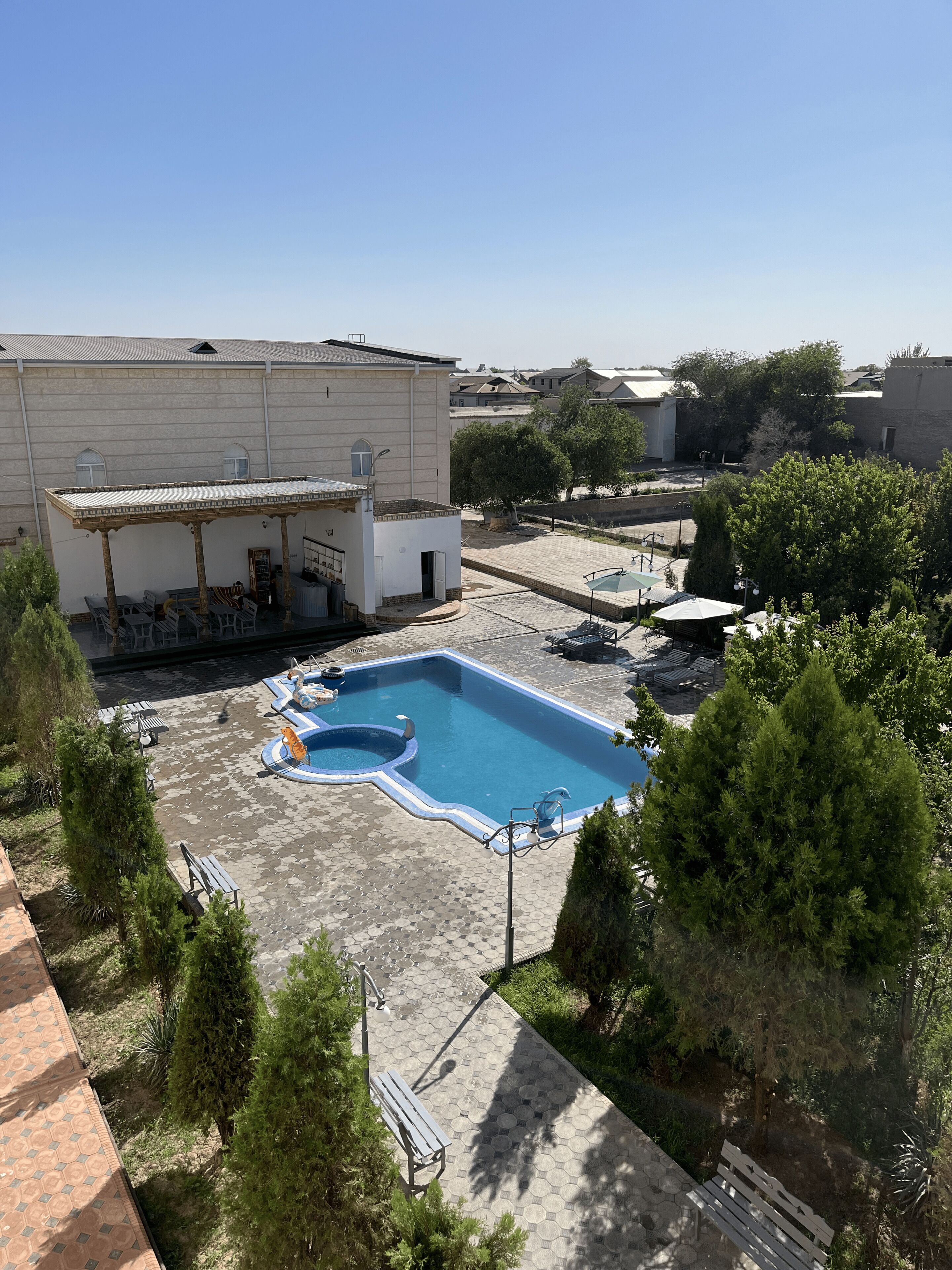 Una piscina en la azotea con un área de descanso cubierta, rodeada de árboles y edificios.