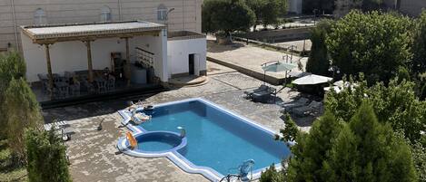 Una piscina en la azotea con un área de descanso cubierta, rodeada de árboles y edificios.