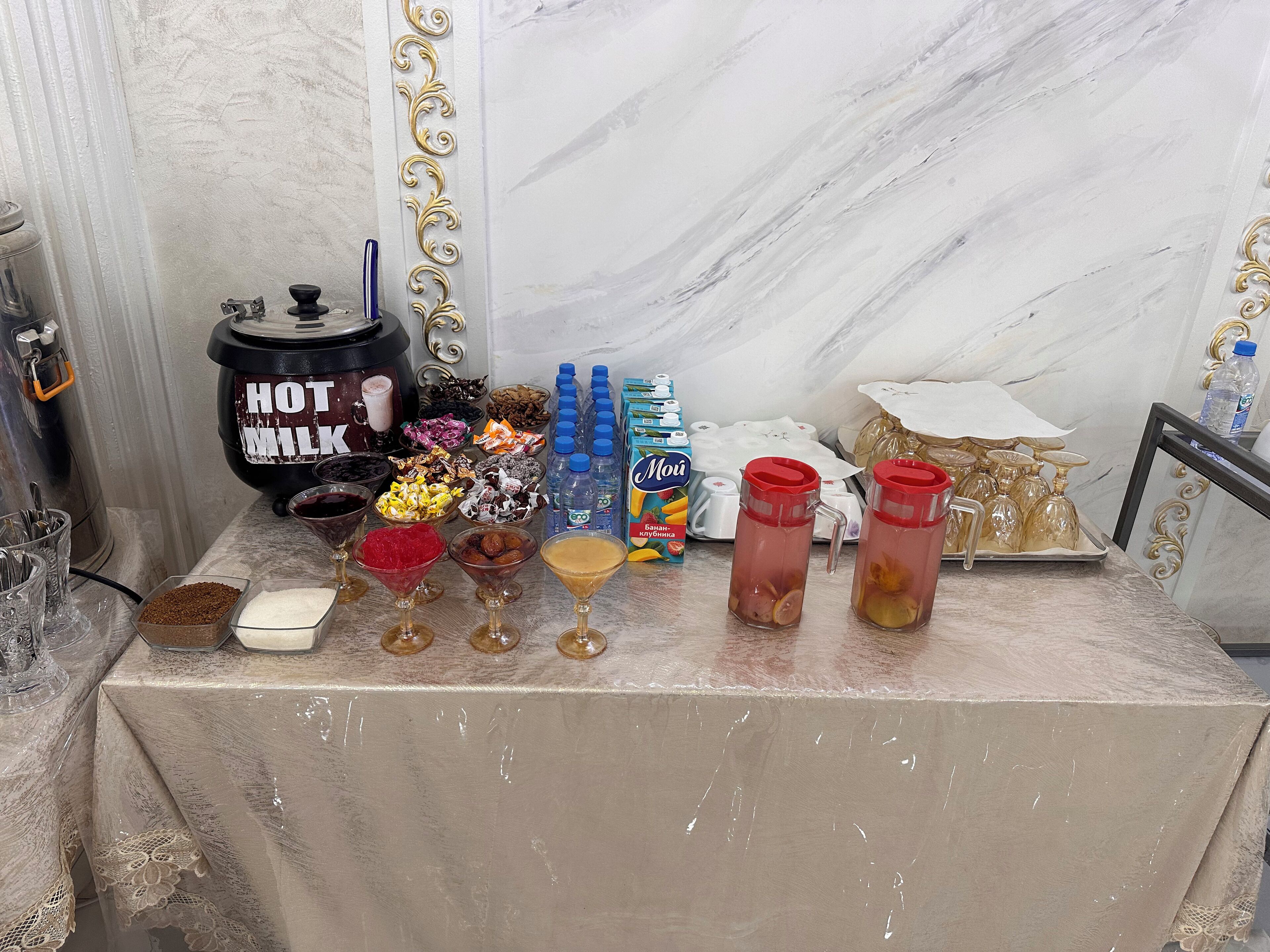 A table with various food items, a hot milk dispenser, and water bottles.