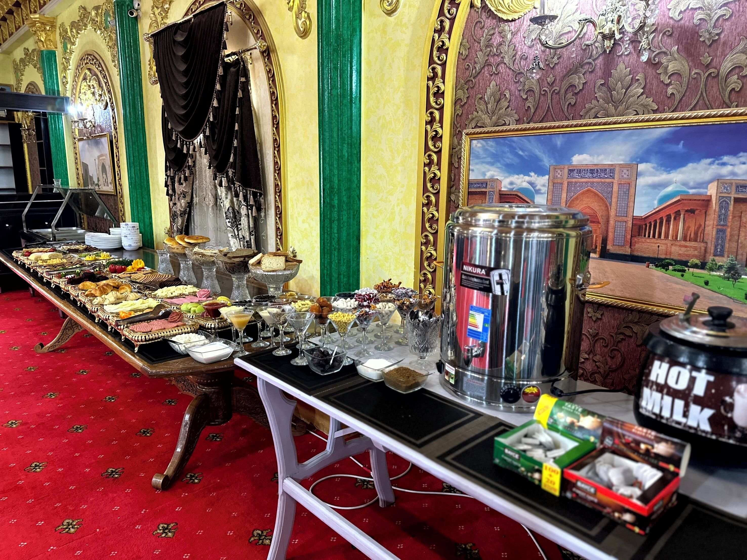 A buffet table with various food items and beverages, a water dispenser, and a hot milk container.