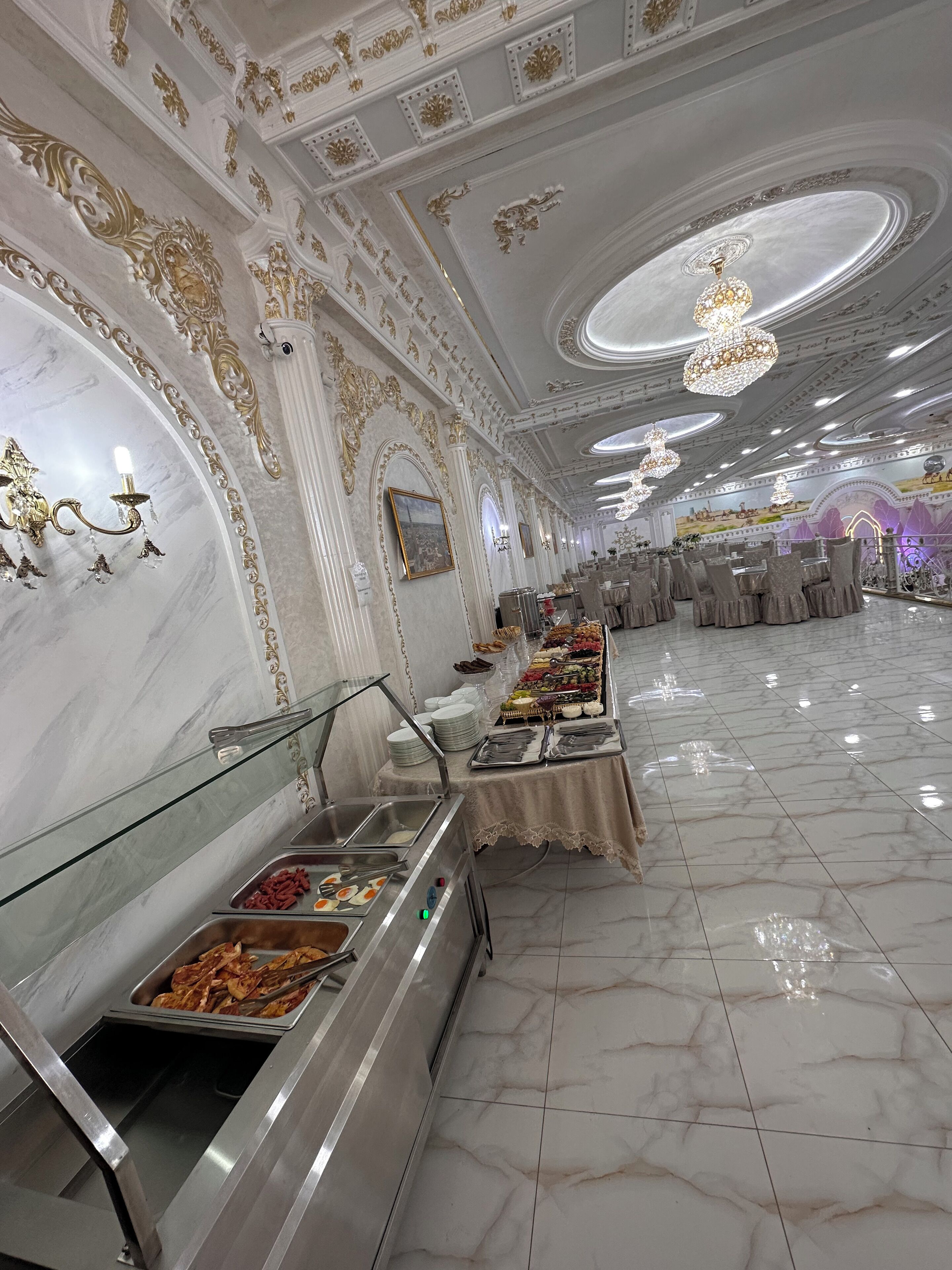 A banquet hall with marble floors, buffet stations, and ornate ceiling decorations.