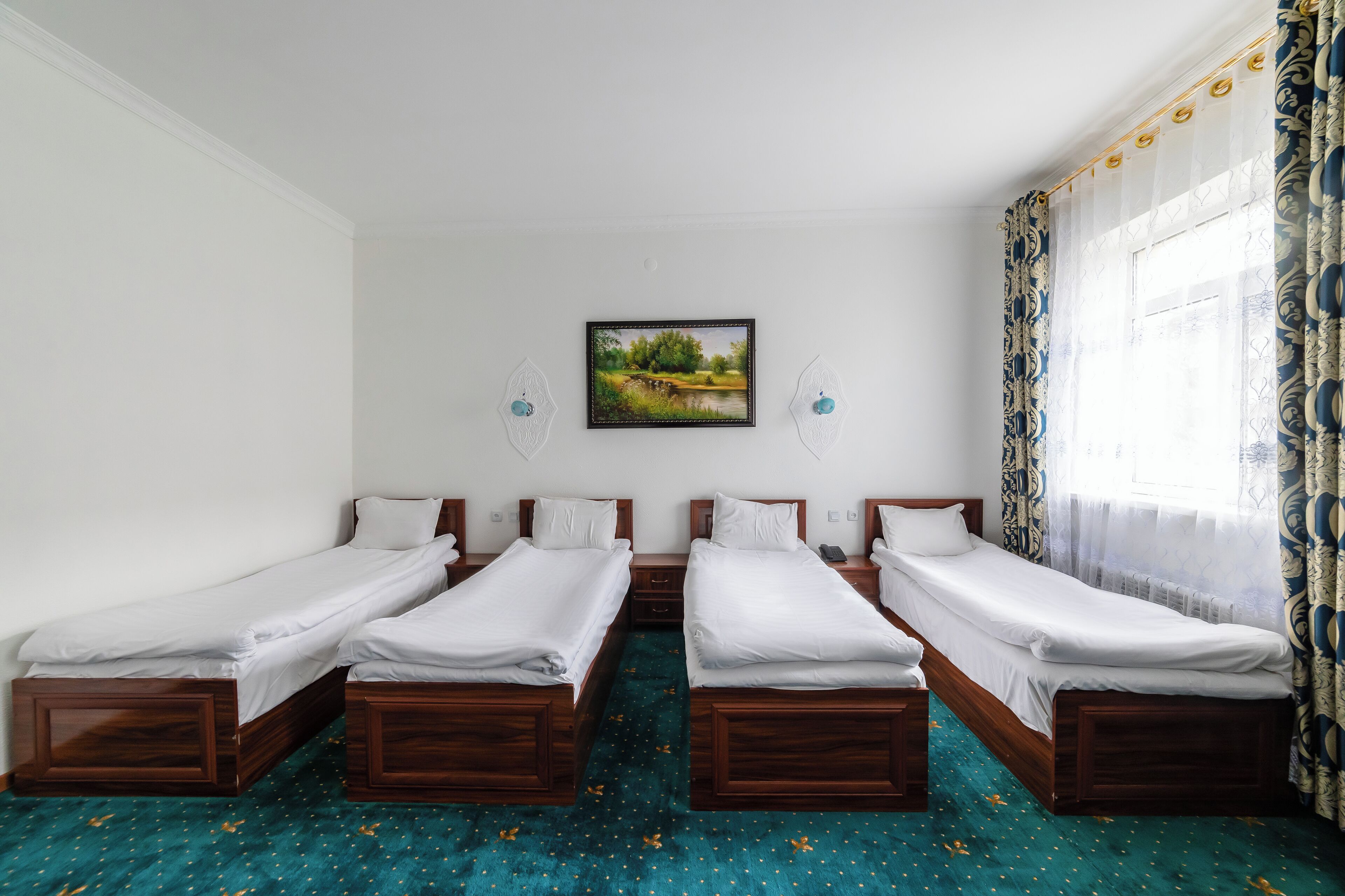 A room with four single beds, a painting on the wall, and a window with curtains.