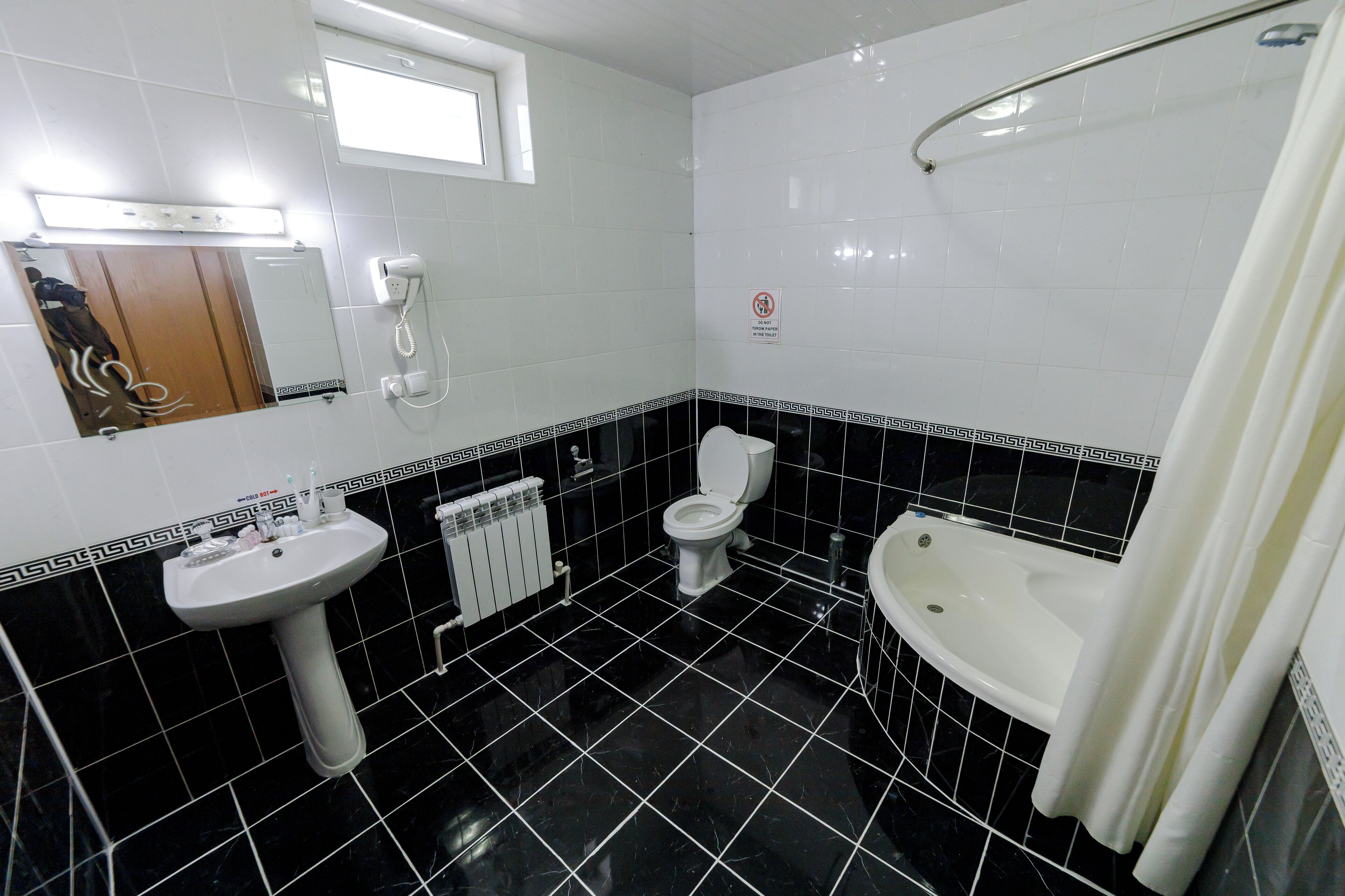 A bathroom with a toilet, sink, and bathtub, featuring black and white tiles and a mirror.