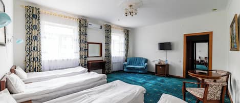 Una habitación de hotel con tres camas individuales, un sillón azul, una mesita de madera, una mesa redonda con una silla y un espejo grande.