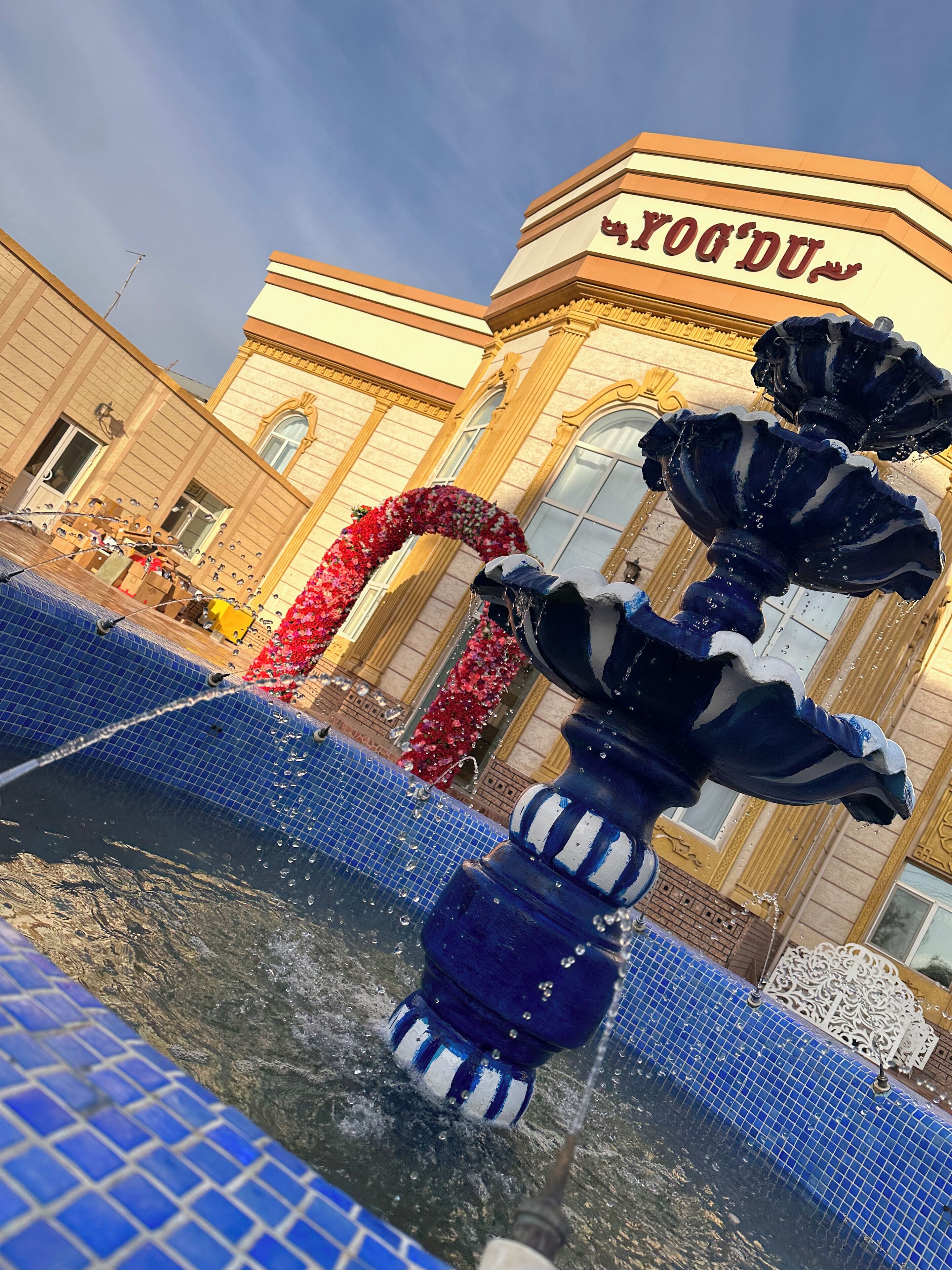 A fountain with water jets in front of a building with a sign that reads "Yogandu."