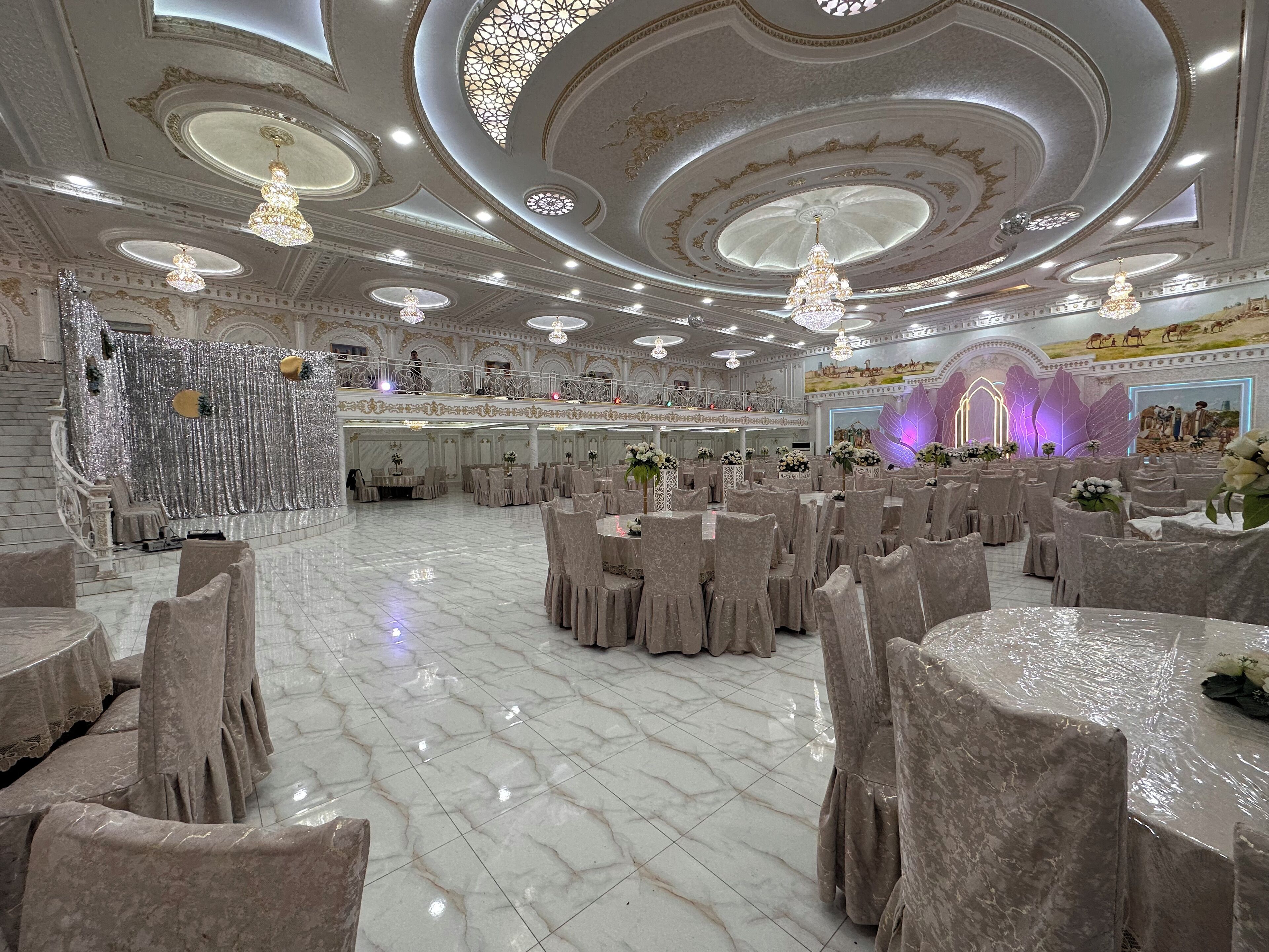 Un gran salón de banquetes con suelos de mármol, candelabros ornamentales y un decorado llamativo.