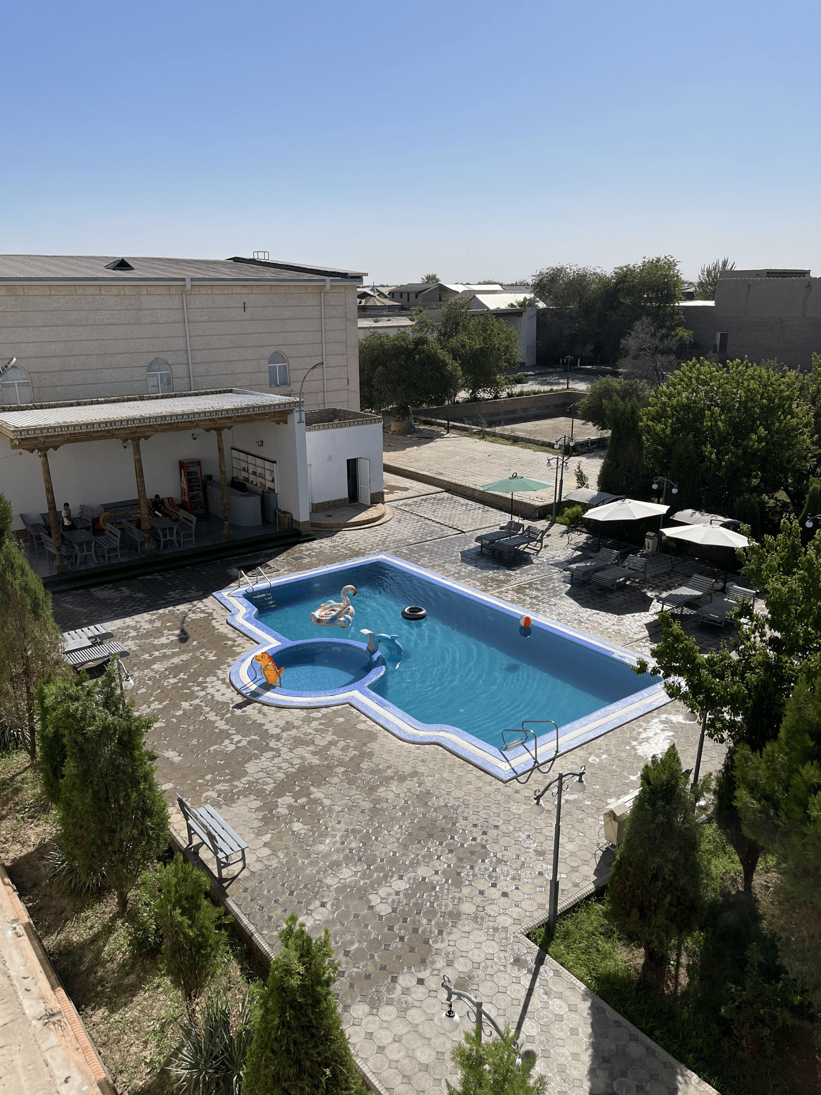Una piscina con borde ondulado, rodeada por un patio con sillones de descanso y sombrillas.