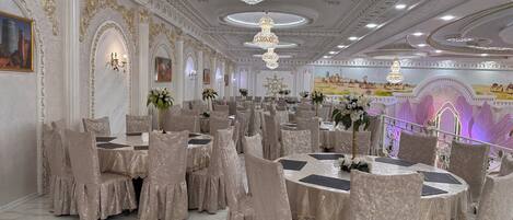 A banquet hall with round tables, covered chairs, and chandeliers.