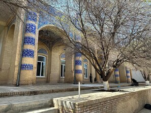 A courtyard with a tiled building featuring arches and blue patterns. - Qibla Tozabog (Khiva)