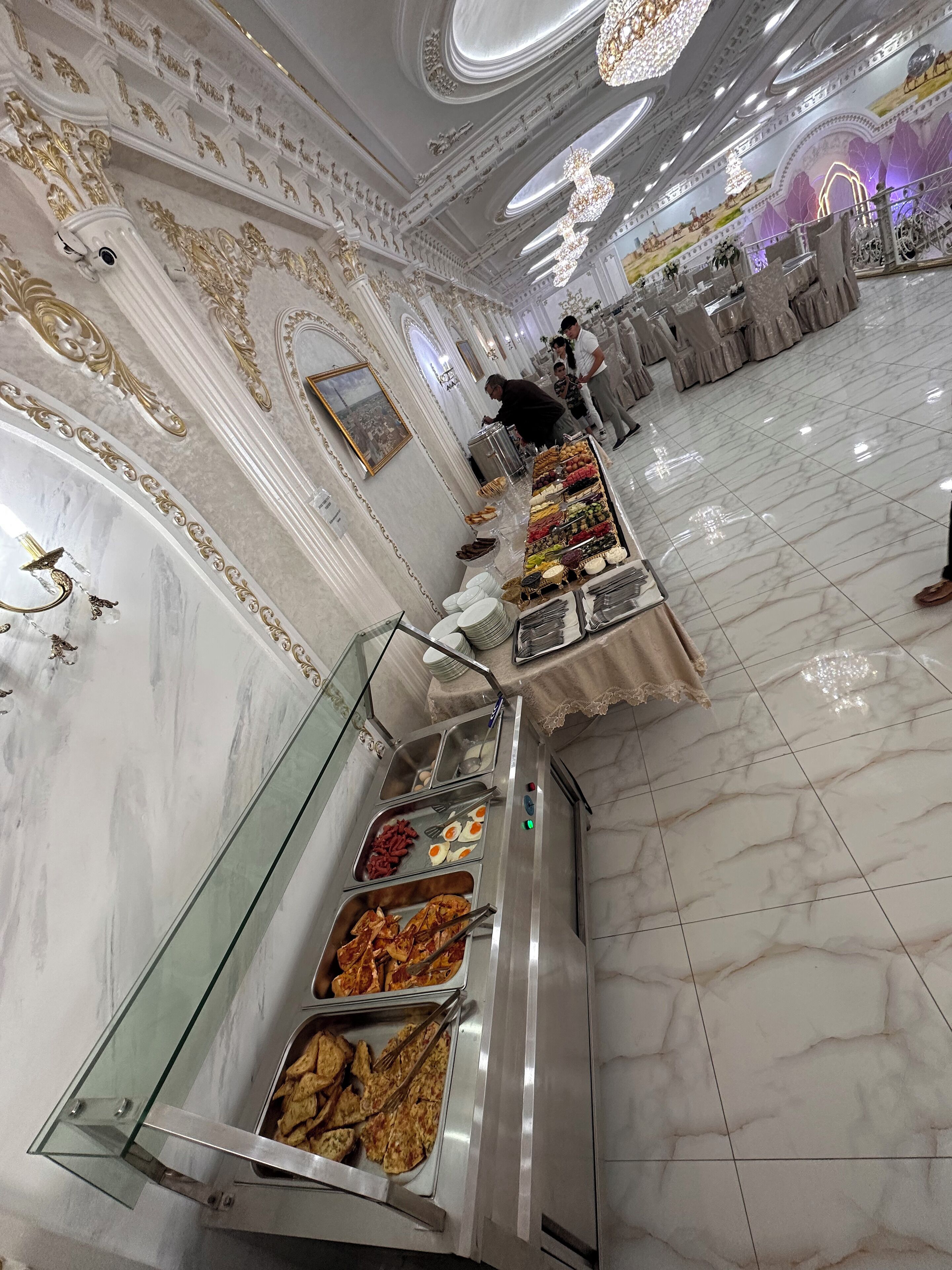 Een buffetgedeelte met diverse gerechten, marmeren vloeren en versierde wanddecoraties.