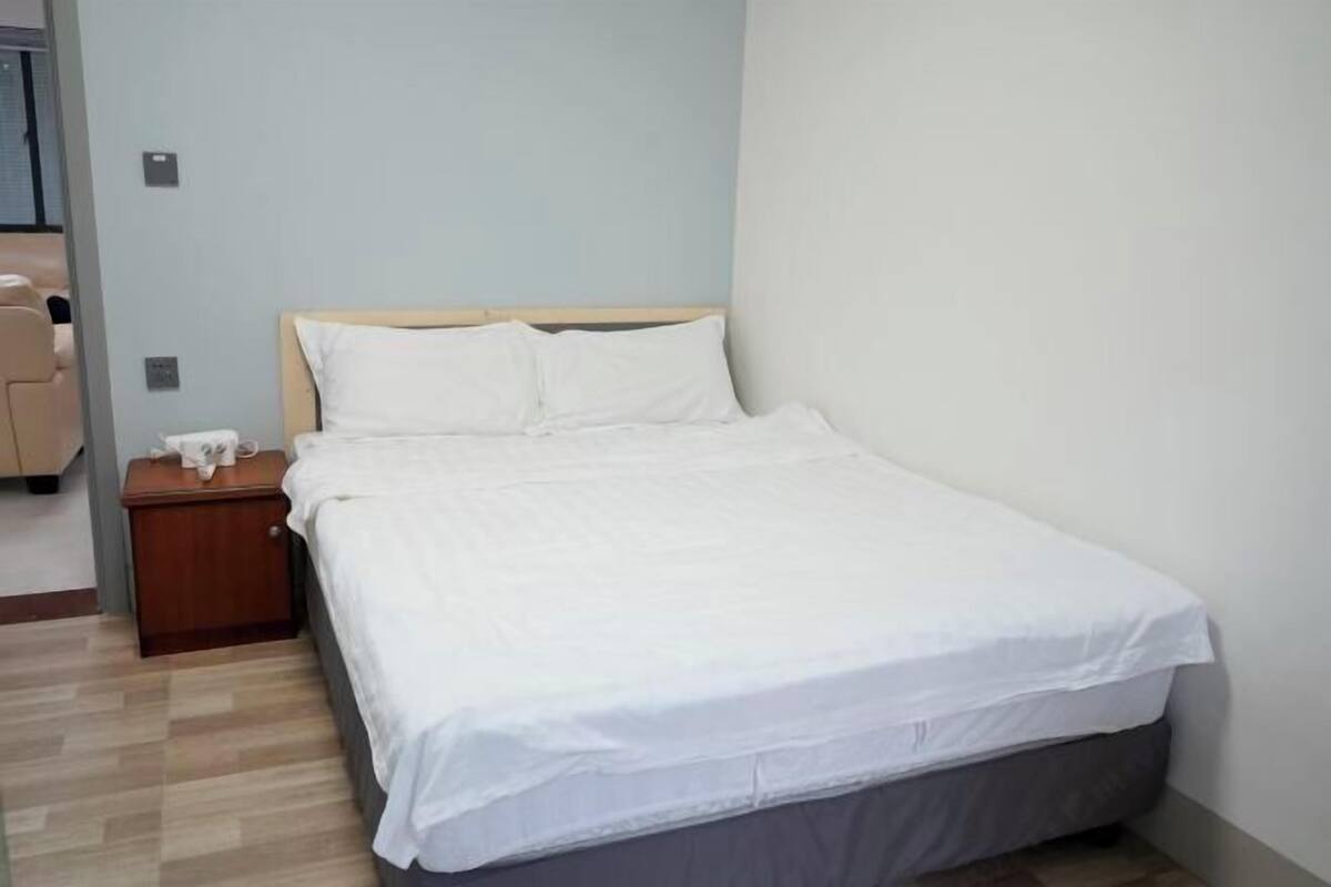 A single bed with a wooden headboard, a bedside table with a lamp, and a plain wall.