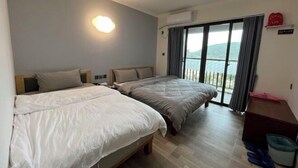Habitación de hotel con dos camas, un balcón con vistas y un escritorio pequeño con un cesto de basura.